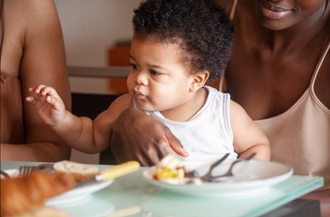 A mum enjoying a cafe coffee and meal with other parents. Her baby sits on her lap and looks around.
